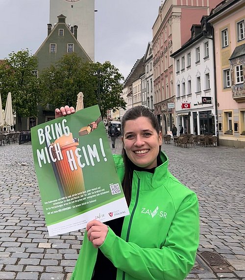 Mitarbeiterin zeigt Plakat gegen Vermüllung mit dem Titel "bring mich heim"