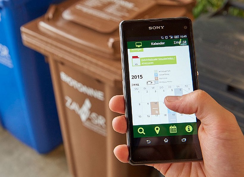 Handy mit der geöffneten ZAW-SR App und Mülltonnen im Hintergrund