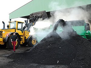 Fronlader füllt frischen Kompost in eine Siebanlage. Am anderen Ende des Geräts kommt der dampfende Kompost wieder heraus. 