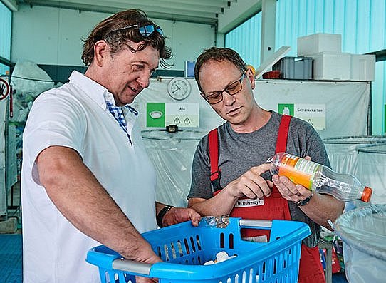 Wertstoffhof-Mitarbeiter und Kunde beim Sortieren von Verpackungsabfällen