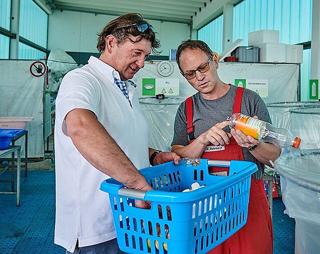 Wertstoffhof-Mitarbeiter und Kunde beim Sortieren von Verpackungsabfällen