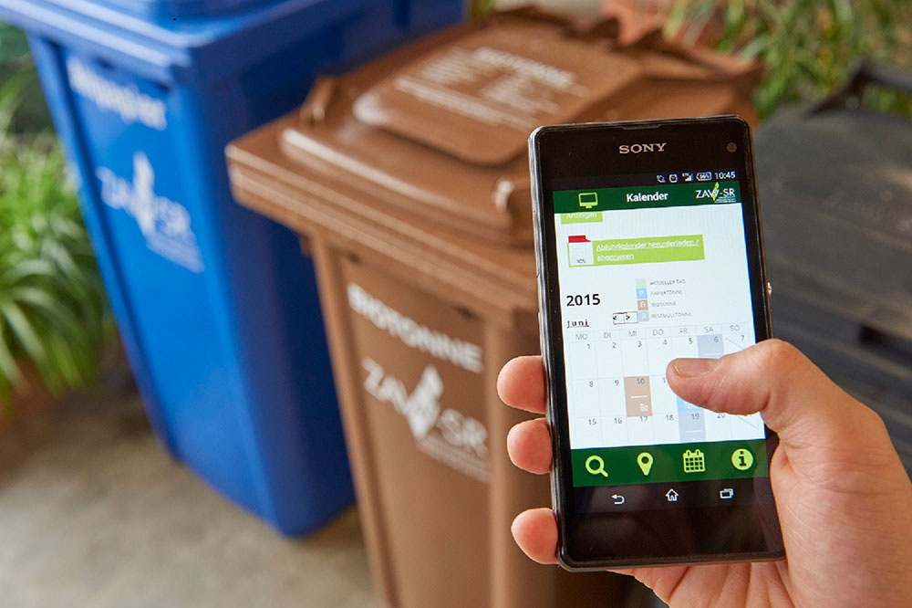 Handy mit der geöffneten ZAW-SR App und Mülltonnen im Hintergrund