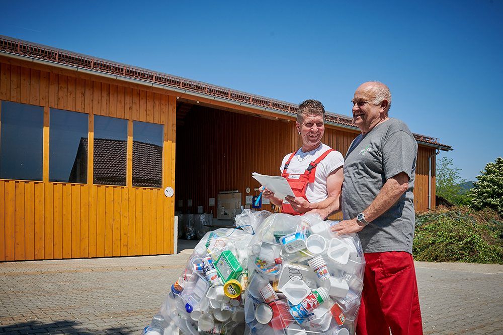 Zwei Wertstoffhof-Mitarbeiter mit Säcken voller Kunststoffverpackungen